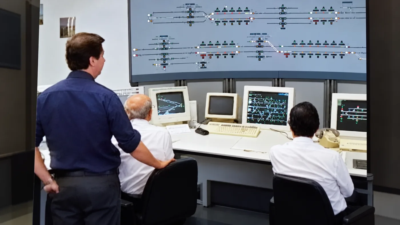 Operatori in una sala di controllo ferroviaria davanti al quadro sinottico e ai monitor